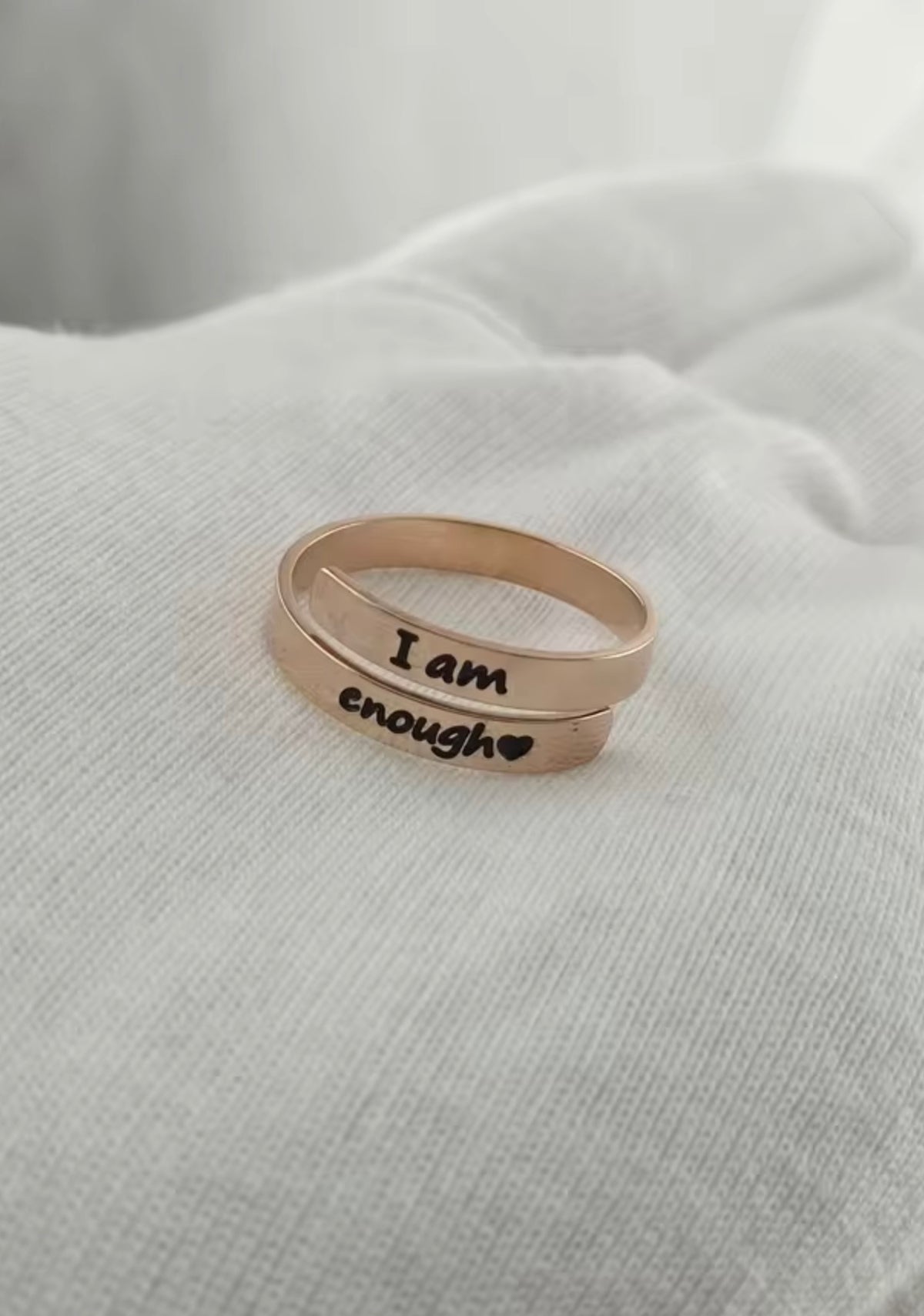 Rose gold I Am Enough ring resting on soft white fabric