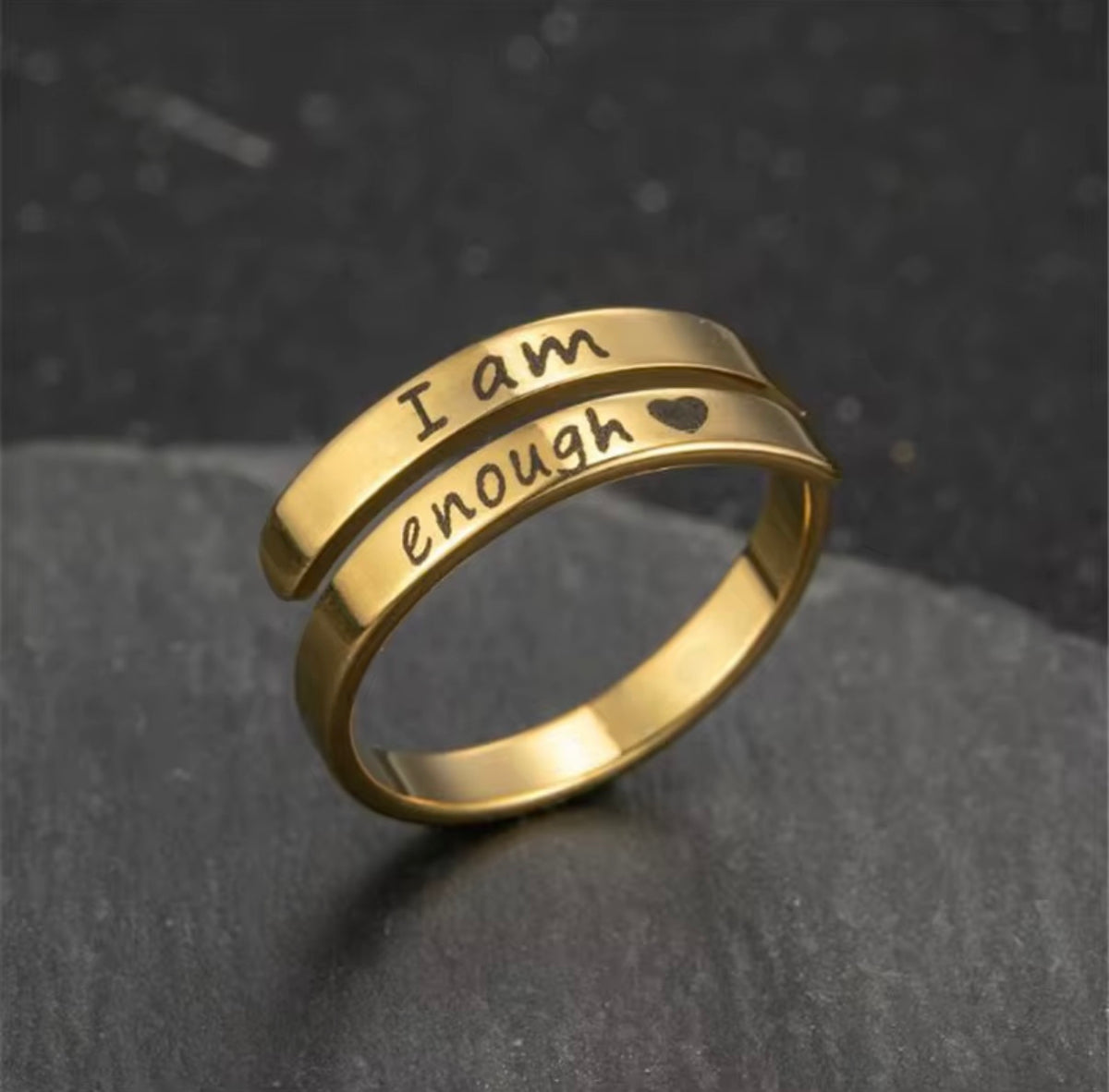 Gold I Am Enough engraved ring on a dark stone surface